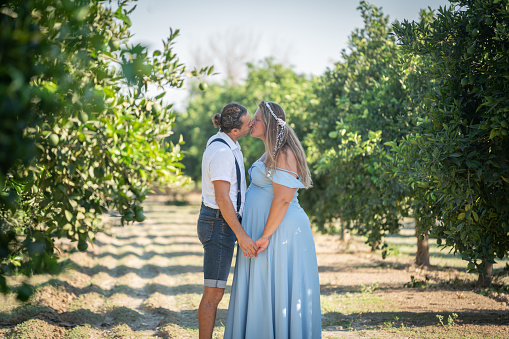 Pregnant woman and her loving man kissing at the orange garden in spring