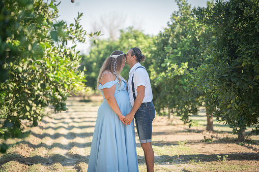 Pregnant woman and her loving man kissing at the orange garden in spring