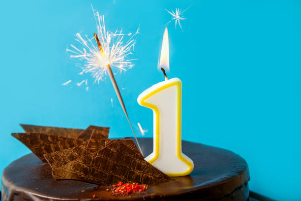 Number 1 birthday candle burning and sparkler with sparks fly on cake. The first birthday of anniversary celebration concept. Lot of copy space on blue background. stock photo