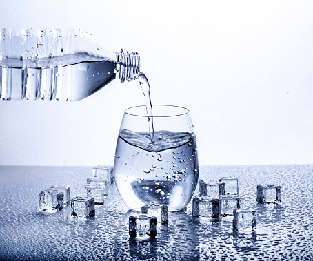 Pouring fresh drinking mineral water from plastic bottle. Glass filled with water over white background.