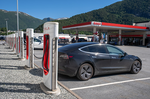 Andalsnes, Norway - June 30, 2022: A static shot of a solid black Tesla Model 3 dual motor charging at the Andalsnes Supercharger in a sunny summer day. Selective focus