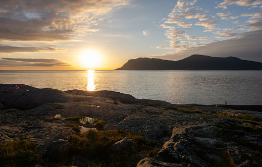 Wonderful landscapes in Norway. Vestland. Beautiful scenery of a sunset on a calm sea in a sunny day with sunrays through the clouds and a fisherman on the shore. Yellow sky and rocks. Selective focus