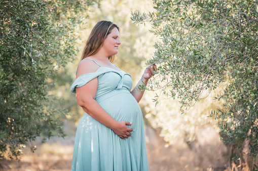 Photo of pregnant woman resting in nature under olive trees