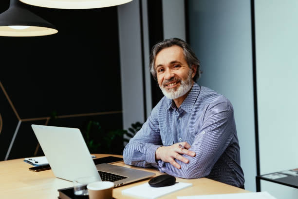 istock Gray hair employee working in office, looking at camera and smiling 1425872253