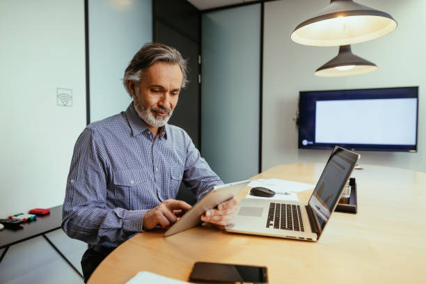 istock Gray hair employee working in office, using digital tablet and laptop 1425872278
