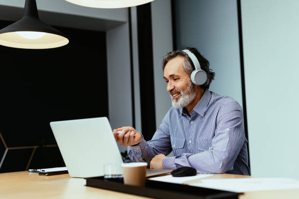 istock Mature businessman working in office, using headphones while attending online meeting 1425872315