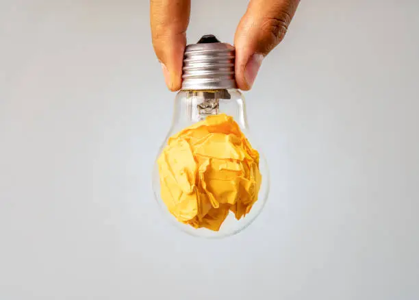 Close up photo of crumbled colorful paper and light bulb in the same frame as a symbol of persistance, perseverance and hardwork. Concept of creative idea , brainstorm and innovative thinking.