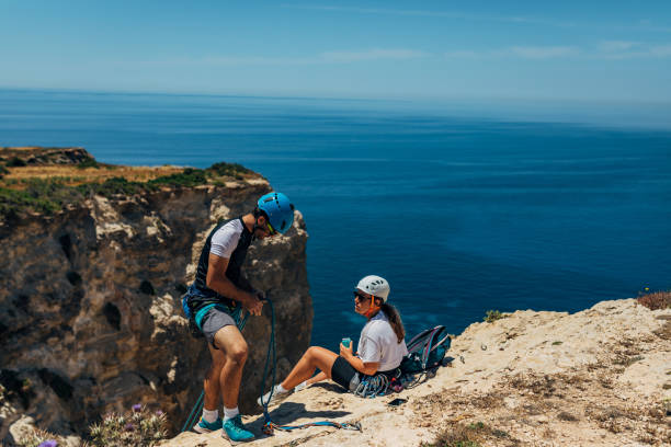 istock A male climber prepares his ropes for descent from a mountain, while a female climber drinking juice from a can 1425879447