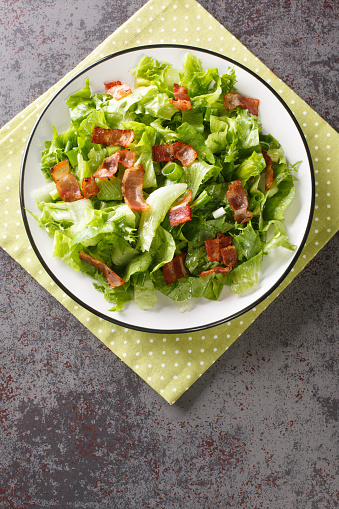 Classic Wilted Lettuce Salad With Bacon Dressing closeup in the plate on the table. Vertical top view from above
