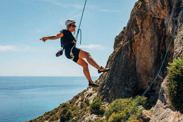 mujer milenaria bajando del acantilado después de escalar rocas. escaladora con casco haciendo rappel por un acantilado empinado - rápel fotografías e imágenes de stock