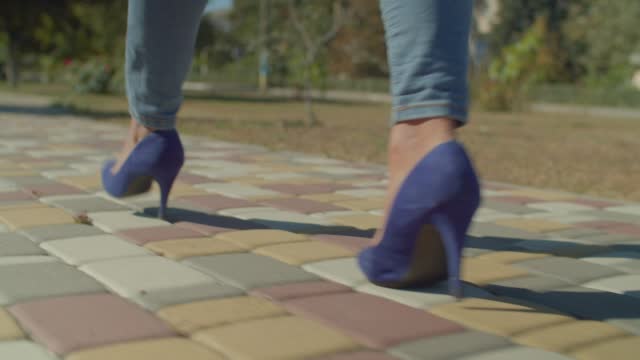 Rear view of slim black female legs wearing stylish heels walking on street