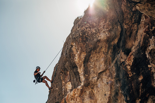 A woman who is a fan of extreme sports uses a rope to climb the steep cliffs of the mountain