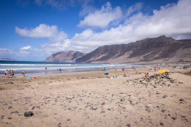 famara strand auf der insel lanzarote, spanien. menschen, die am strand baden. im wasser surfer. - famara stock-fotos und bilder