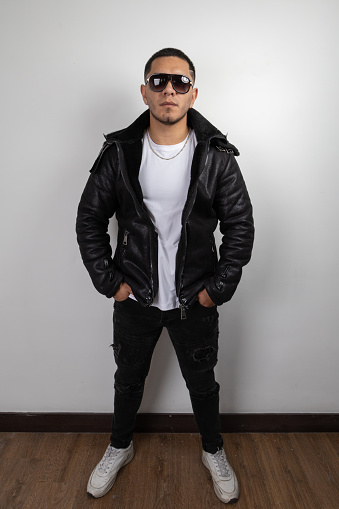 full body of young man with short hair wearing sunglasses, leather sweater, white t-shirt and jeans, casual urban fashion and style, studio