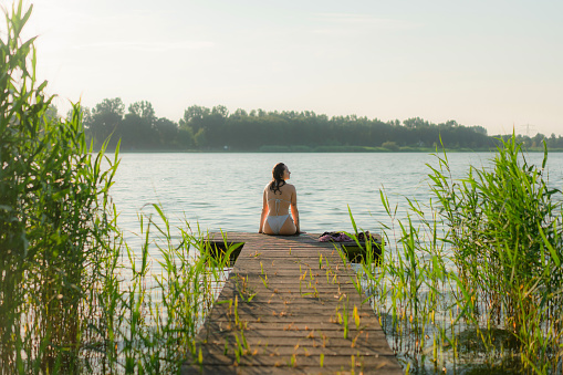 Young Caucasian woman sitting on pier at the lake in summer
