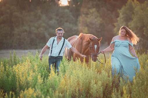 Happy mid adult couple riding their horses outdoors in nature at sunset.