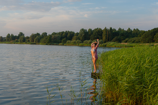 Young Caucasian woman standing on pier on the lake in summer