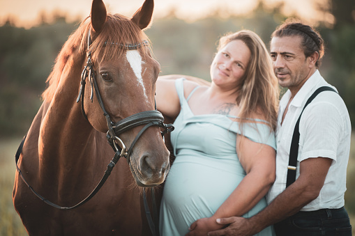 Pregnant woman and her partner spending happy time with their horses in nature