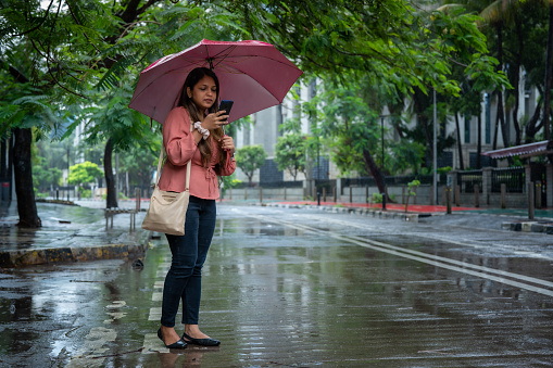 Young Indian woman holds and uses mobile phone on the street in Mumbai while waiting for a taxi