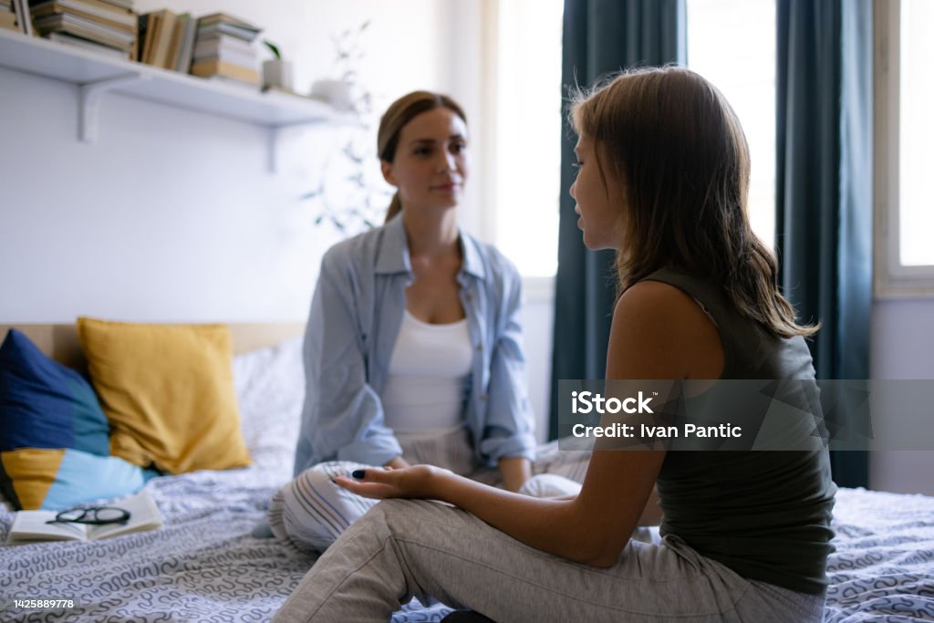Mother and daughter talking at home Middle aged mother sitting on the bed with her daughter, listening to her teenage problems and trying to help her with conversation Teenager Stock Photo