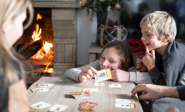 Sister and brother are playing cards with the family at home on Christmas holidays Portraits of smiling and laughing Siblings playing tabletop game at home with Christmas decorations and fire in a chimney family playing card game stock pictures, royalty-free photos & images