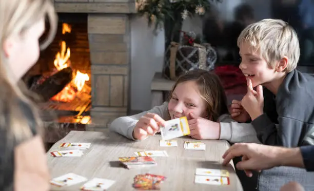 Portraits of smiling and laughing Siblings playing tabletop game at home with Christmas decorations and fire in a chimney