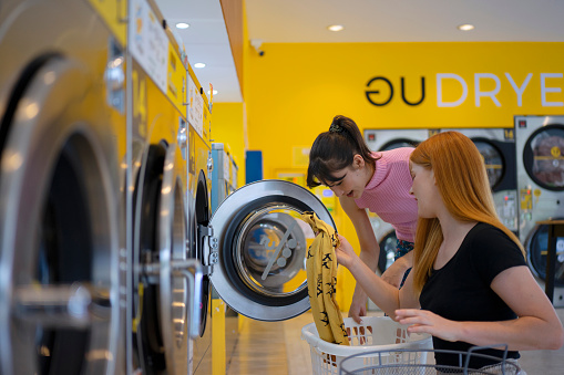 ํYoung women are bring their cloths to wash at Launderette.  Coin washing machine, coin laundry and self service concept.