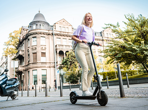 Young Caucasian albino woman riding electric scooter. She is dressed in casual summer clothes. Exterior of urban city street during the day.