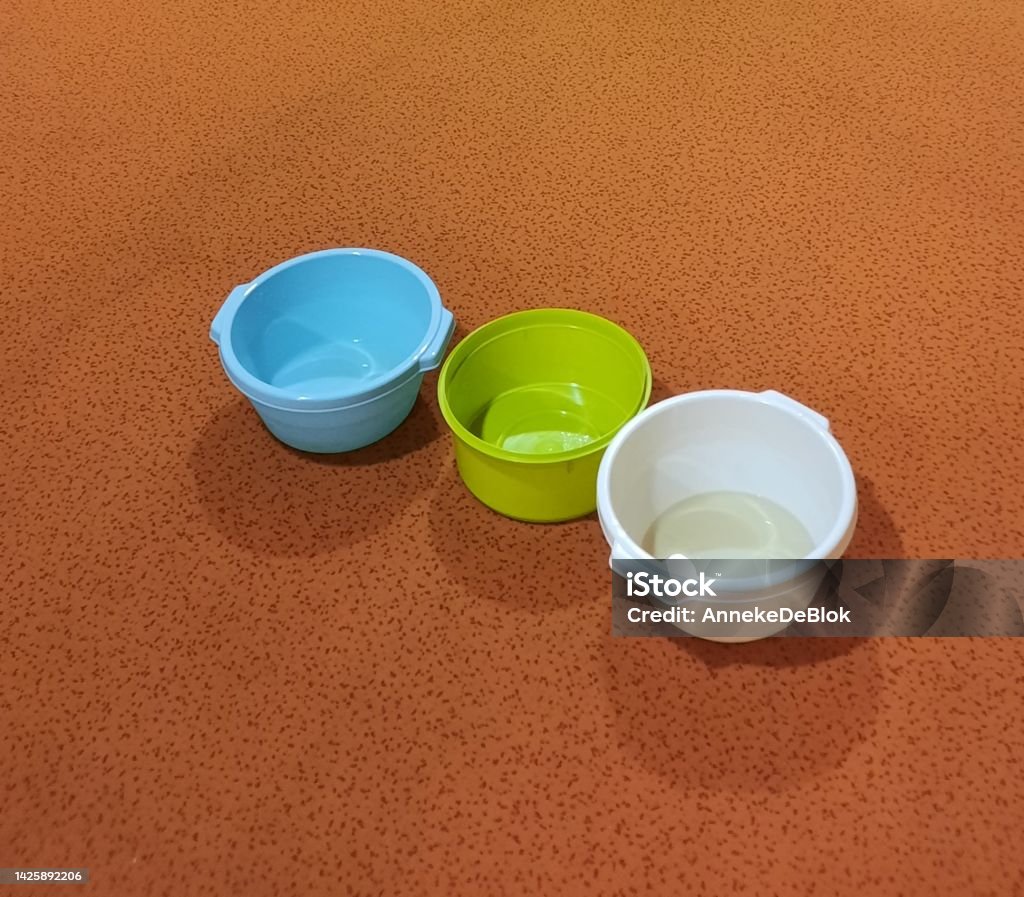 Washing-up bowls with water for a leak int the ceeling Three plastic washing-up bowls to collect the water from a leaking ceeling in a house. placed on the floor on an orange carpet. Blue Stock Photo