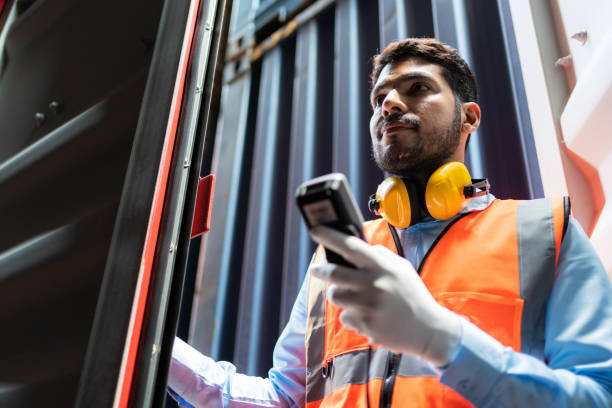 istock Dock worker man in safety vest holding barcode scanner inspector the quality of container at shipping yard. Logistic and Transportation, Global Business concept. Cargo freight ship for import export 1425895952