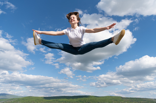 full of energy. gymnast warming up on sky background. flexibility. child training at school physical education lesson. freedom in motion. stamina. teenage girl jump in split.