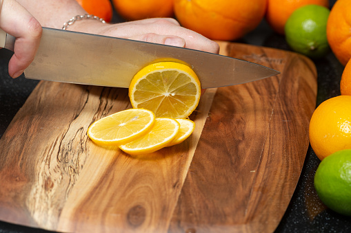 Women's hands cut juicy lemon into thin slices on a board