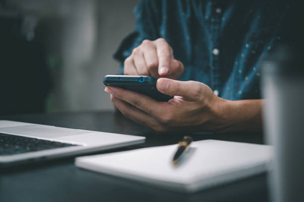 istock Man holding a phone with a pen and paper to write a note in an office diary using a laptop at office. 1425898692