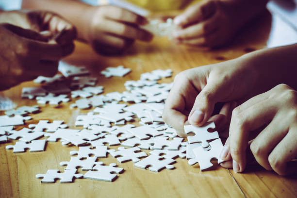 Hands of a person little child and parent playing jigsaw puzzle piece game together on wooden table at home, concept for leisure with family, play with children's development, education and fun. stock photo