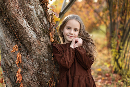 Smiling baby girl in dress with long hair in fall park. Closeup portrait child praying. Little girl hand praying, hands folded in prayer concept for faith, spirituality and religion.