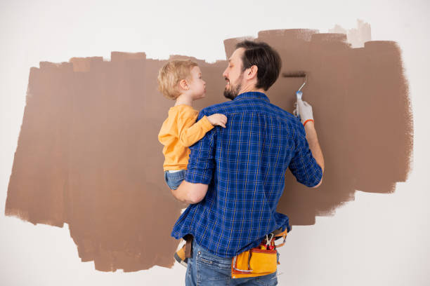 um pai segura seu filho pequeno em seus braços e juntos eles desenham nuvens em marrom. a criança está usando uma blusa laranja, e o homem está usando uma camisa xadrez azul. a foto é tirada de trás - brown hair caucasian little boys men - fotografias e filmes do acervo