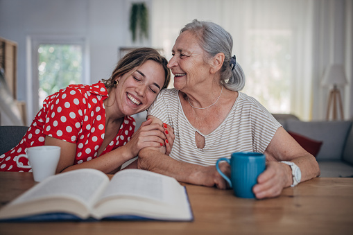 Cheerful granny and teenage granddaughter enjoying morning coffee and talking at home