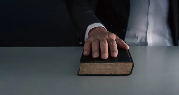 Photo of Hand on black book ,swearing on the bible , concept of telling the truth . on grey blue background .