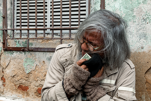 Asian homeless man rejoices after receiving banknotes from passersby to help. man long hair, unkempt beards sit and eat old walls because they have no homes to live in and sleep on city streets.