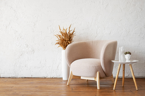 A cozy modern beige armchair against the background of a white empty wall. Interior mockup with copy space.