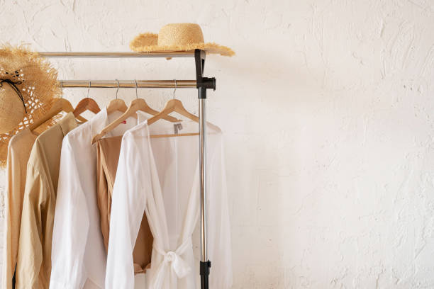 istock Trendy capsule wardrobe in beige and white on a rail rack with straw hats. Copy space 1425918204