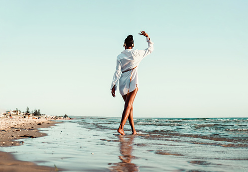 Happy young slim beautiful African woman walking, dancing and having fun at the beach