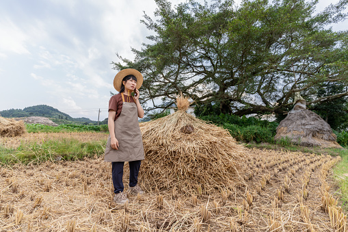 An Asian woman farmer was talking by phone near the haystack