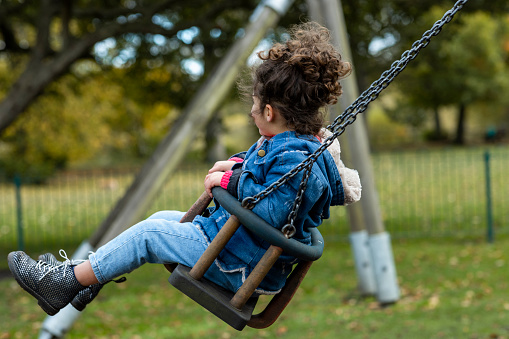 A young girl playing on a push swing at a public park in Hexham, North East England during Autumn. Her face can't be seen.