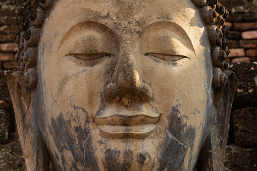Close-up of the eye and face of an ancient Buddha statue in a temple in Sukhothai Historical Park, Thailand