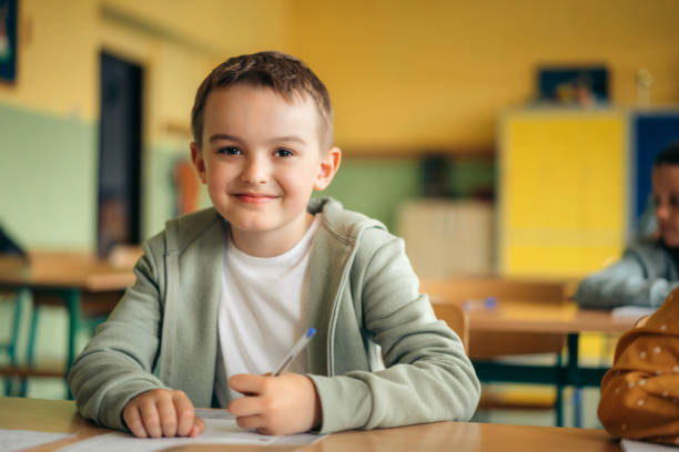 istock elementary schoolboy writing exam at desk in classroom 1425953346