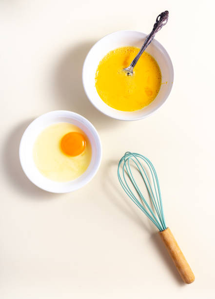 istock Egg beat, Egg Shell with Whisk. Raw eggs in a glass and white bowl on the table. Flat lay. Broken White Background. 1425958537