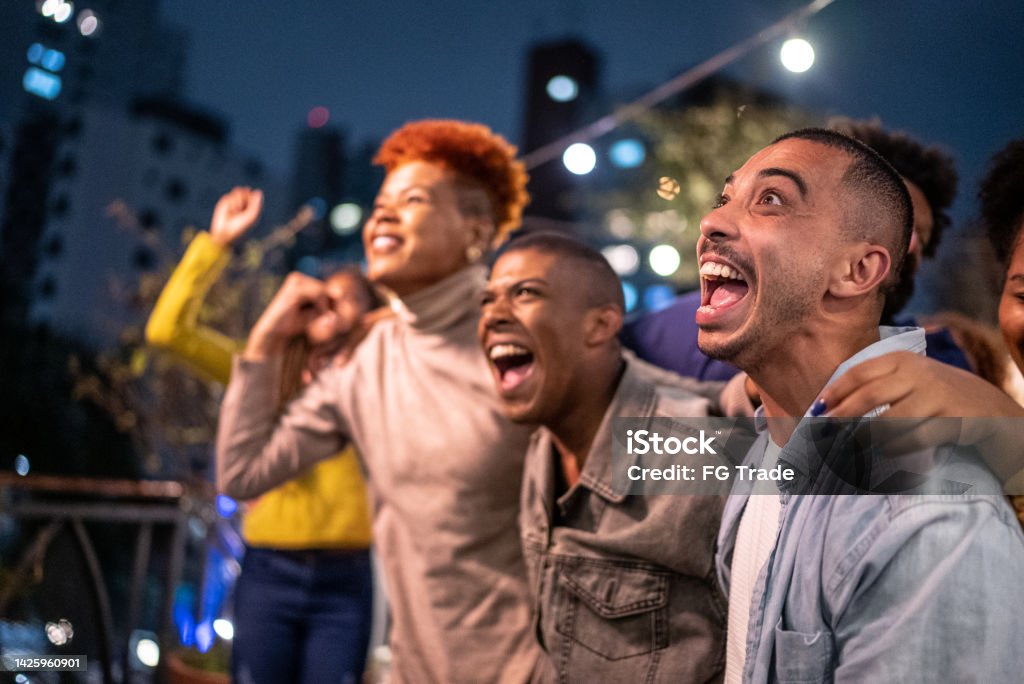 Sports fans watching a match and celebrating at a bar rooftop Fan - Enthusiast Stock Photo