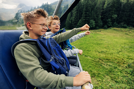 Two teenagers riding on chairlift in the high mountains on a summer day. Vorarlberg, Alps, Austria.\nCanon R5