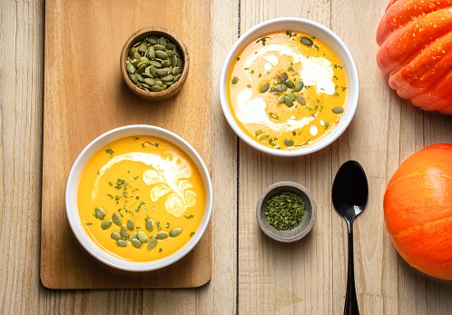 Yellow Pumpkin Soup with cream, pumpkin seed, and parsley on wooden background. Copy space. Top view.